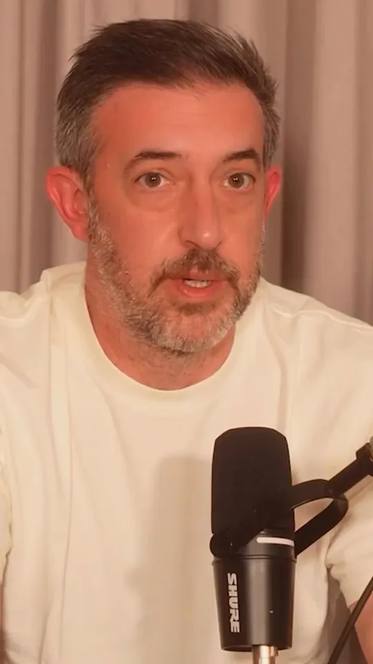 A dad at a podcast microphone, mid-reaction, in an indi t-shirt