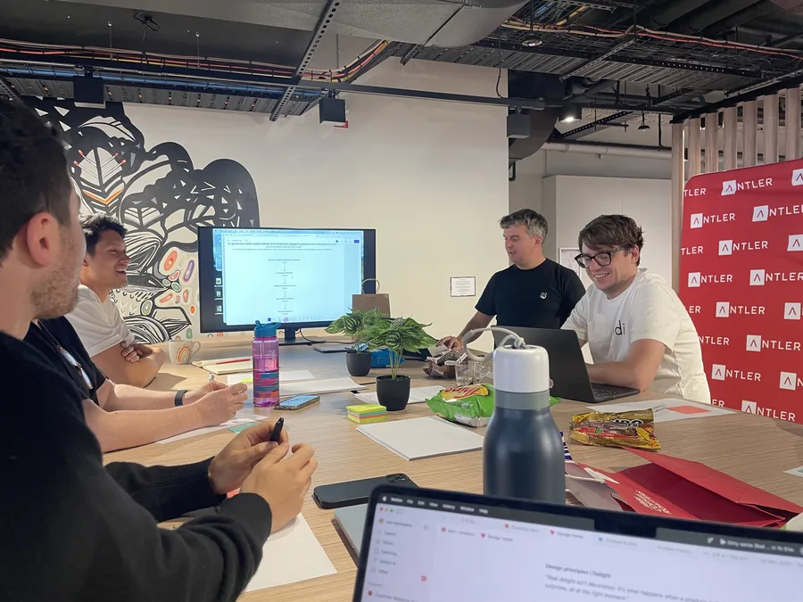 The team around a table at Antler, laughing through an ideas workshop with the agenda up on the screen