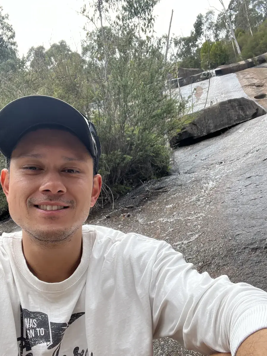 A teammate in a cap on a bushwalk, beside a creek running over a rock slab