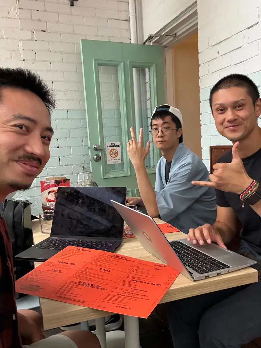 Three teammates working over lunch at a café, laptops open and a menu on the table