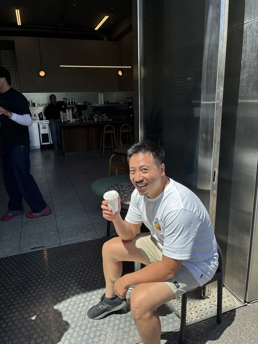 A teammate grinning over a takeaway coffee outside a café