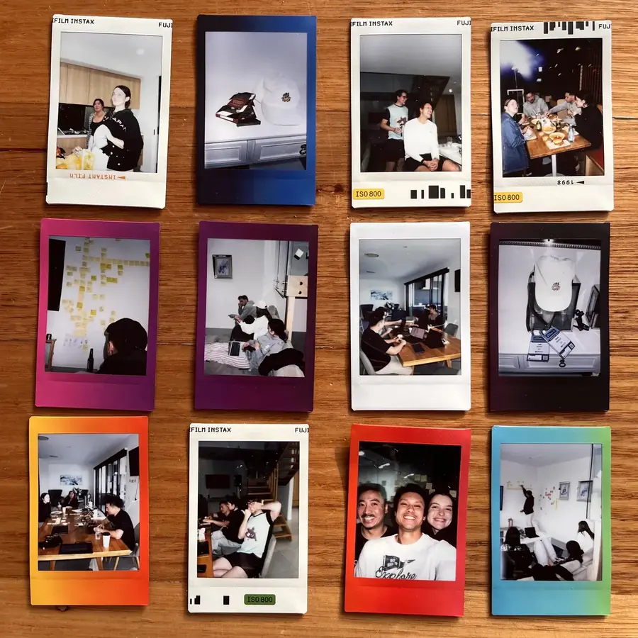 Twelve instant film prints from a team day laid out on a wooden table: dinners, a sticky-note wall, laptops on the couch and indi caps