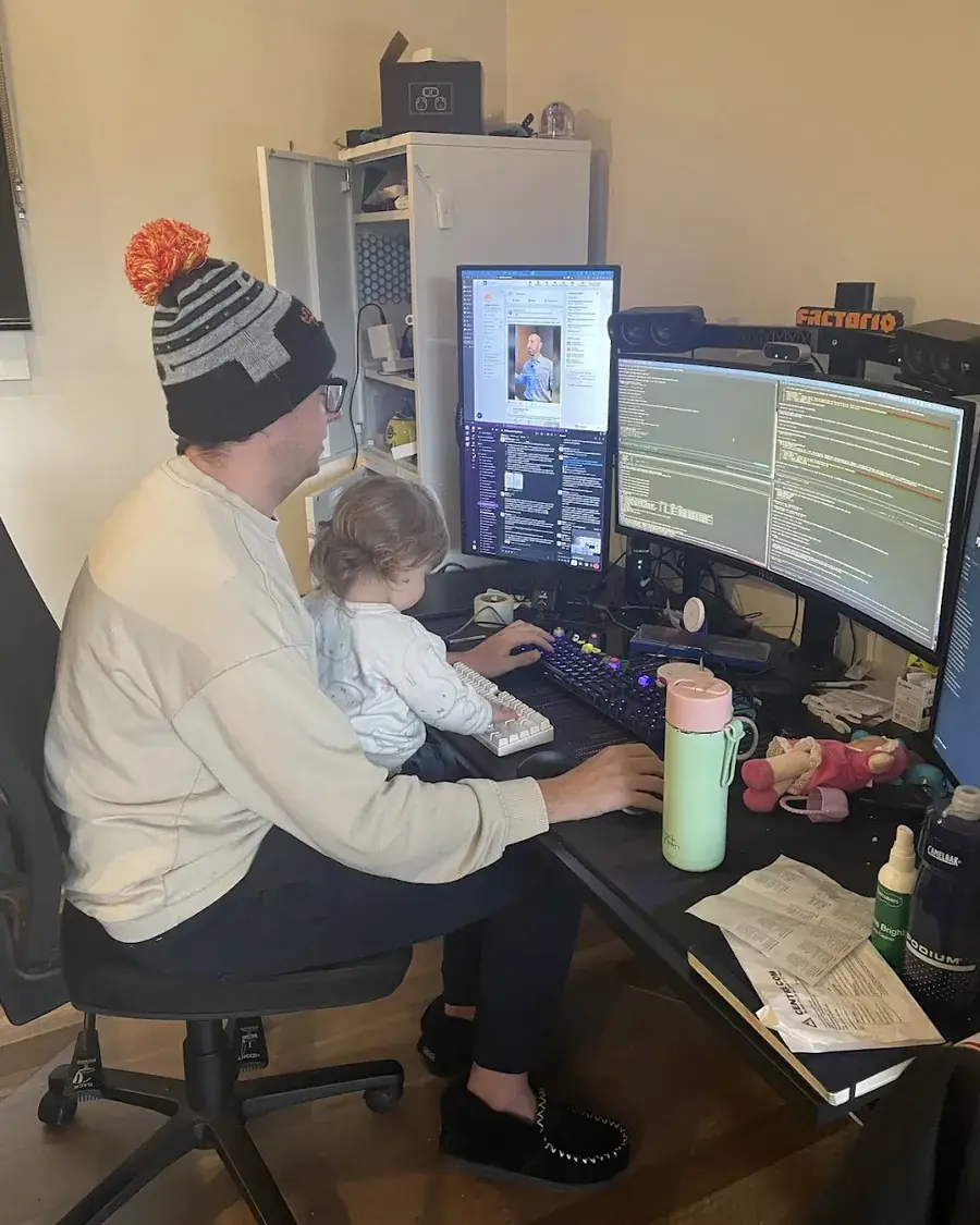 Jordan coding at his desk with a toddler on his lap
