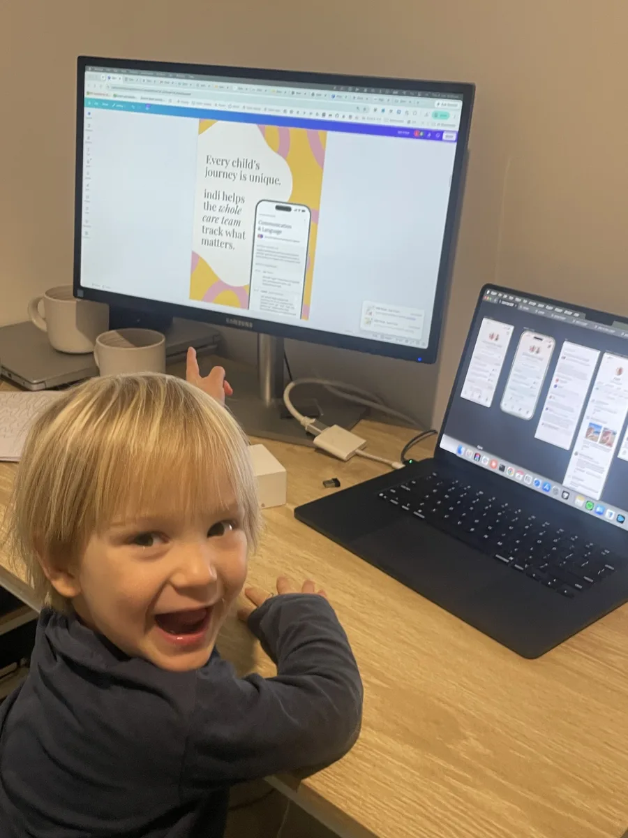 A delighted young boy at a desk, pointing back at an indi poster on the monitor behind him