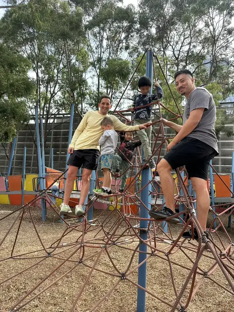 Orrin, a teammate and their kids climbing a rope frame at a playground