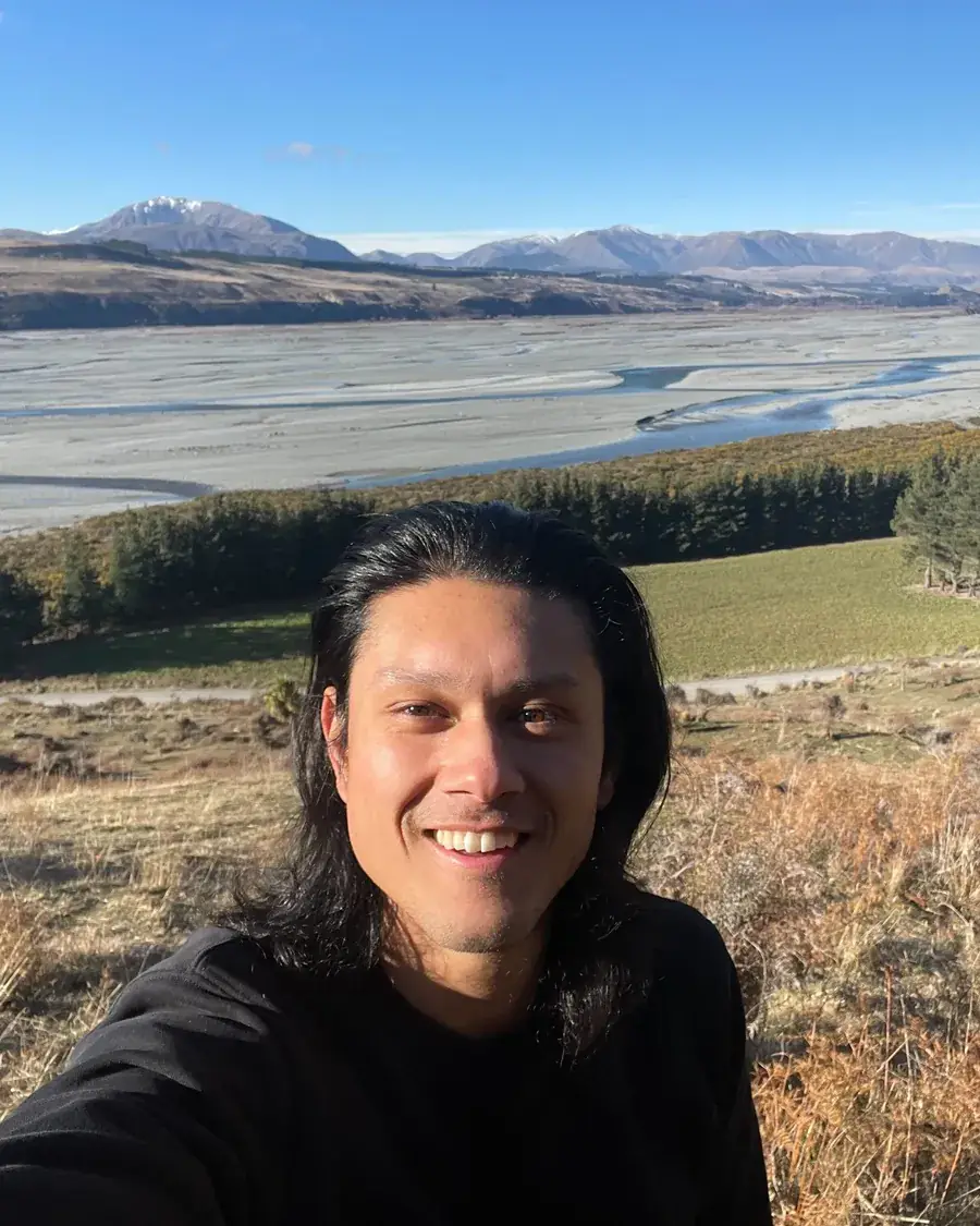 Sing smiling in front of a braided river valley and mountains